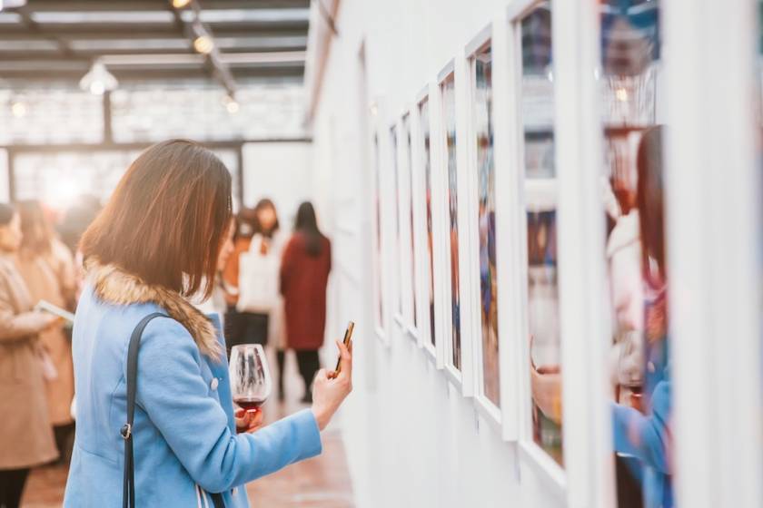 woman at art gallery drinking wine and snapping a photo with her phone